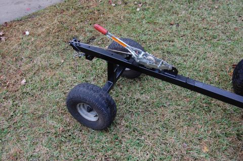2006 Honda RANCHER - A close-up view of a trailer frame, showing its wheels and towing mechanism resting on a grassy surface.