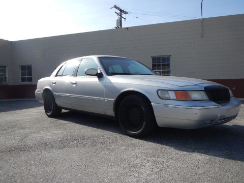 2002 Mercury Grand Marquis - A silver 2002 Mercury Grand Marquis is parked on a gravel lot in front of a brick building.