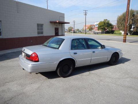 2002 Mercury Grand Marquis - A silver 2002 Mercury Grand Marquis is parked on a paved lot next to a brick building.