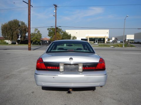 2002 Mercury Grand Marquis - Rear view of a silver sedan parked in an asphalt lot with buildings in the background.