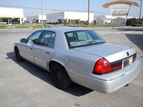 2002 Mercury Grand Marquis - A silver 2002 Mercury Grand Marquis sedan is parked outdoors in front of industrial buildings.