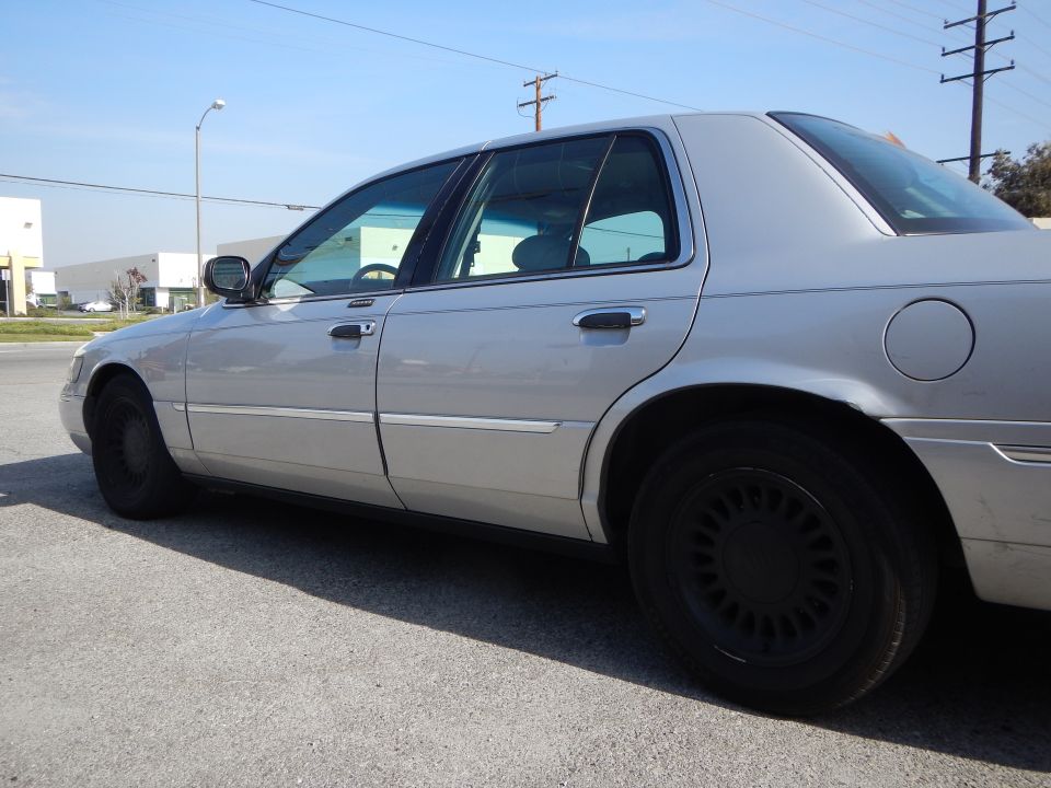 Silver 2002 Mercury Grand Marquis sedan, side view. Black wheels, chrome trim