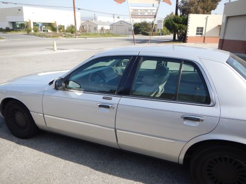 2002 Mercury Grand Marquis - A silver 2002 Mercury Grand Marquis is parked on the side of a street with buildings in the background.