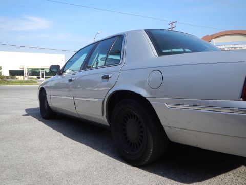 2002 Mercury Grand Marquis - Side view of a silver sedan with black wheels parked outdoors under a clear blue sky.