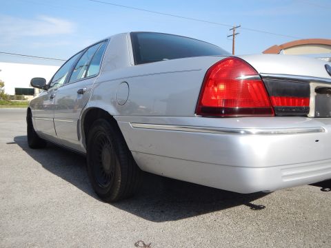 2002 Mercury Grand Marquis - A silver 2002 Mercury Grand Marquis is parked on a sunny day, showing its rear passenger side and a portion of another vehicle behind it.