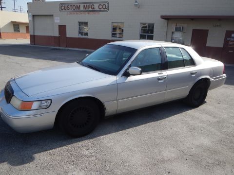 2002 Mercury Grand Marquis - A silver 2002 Mercury Grand Marquis is parked in front of a commercial building with a sign that reads 'CUSTOM MFG. CO. SCREW MACHINE PRODU…