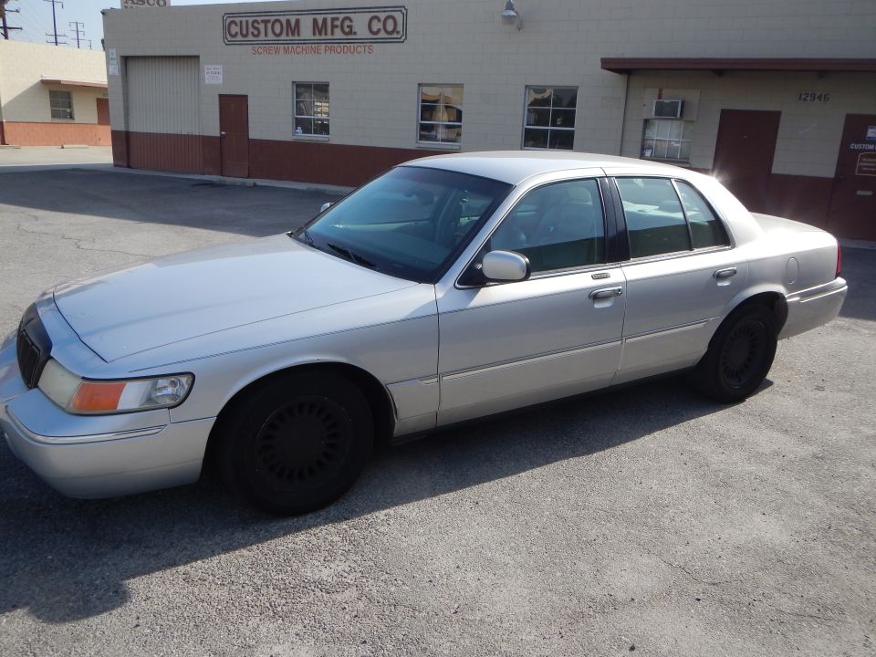 Silver 2002 Mercury Grand Marquis parked outside a building with 'CUSTOM MFG. CO.' sign