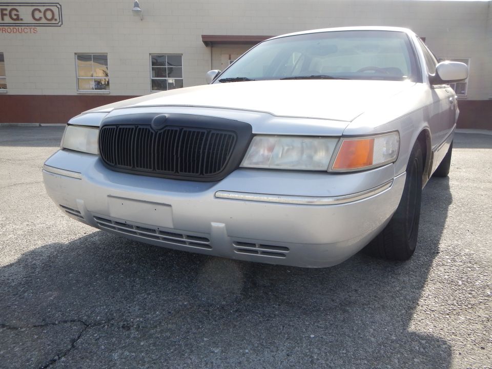 Silver sedan, looks like a Mercury Grand Marquis, parked outside a building. Black grille