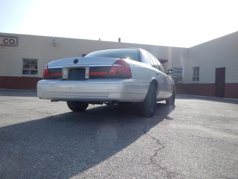 2002 Mercury Grand Marquis - The rear of a silver sedan is shown parked in front of a commercial building under a bright sky.
