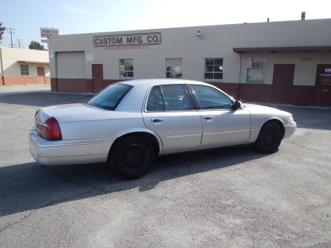 2002 Mercury Grand Marquis - A silver 2002 Mercury Grand Marquis is seen parked in front of a commercial building with 'Custom Mfg. Co.' signage.