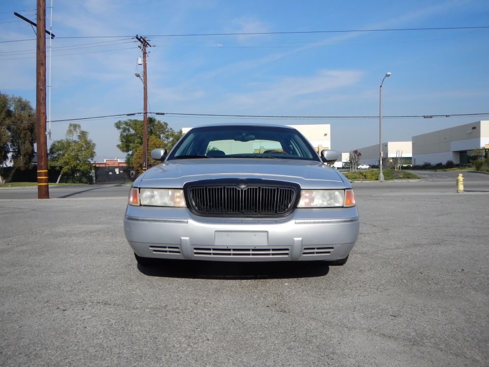 Front view of a silver 2002 Mercury Grand Marquis parked outside with industrial buildings in the background