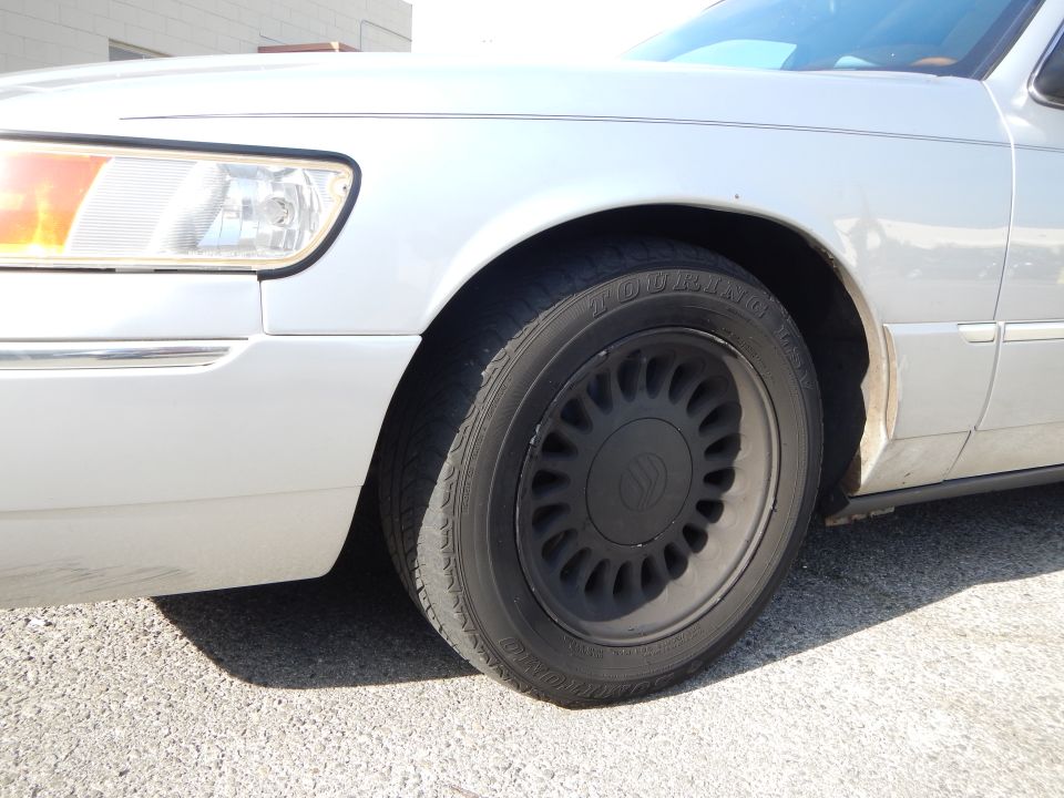 Silver 2002 Mercury Grand Marquis front wheel and fender, showing a black wheel with a chrome lip and a portion of the headlight