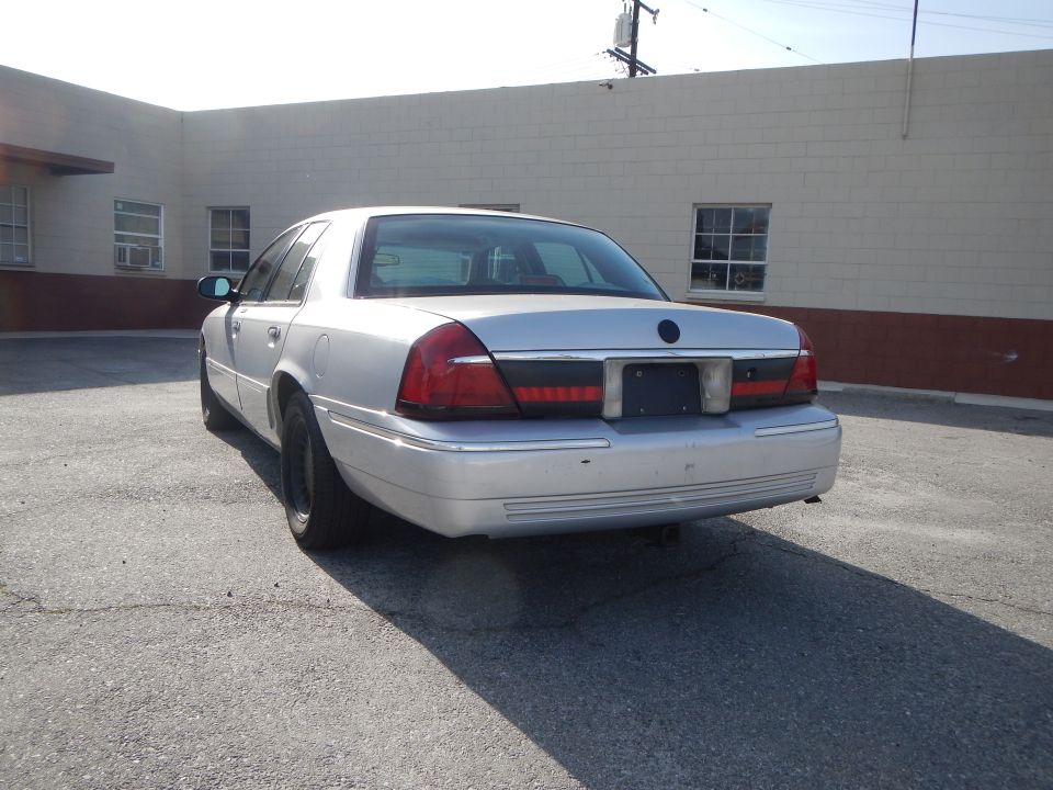 Silver 2002 Mercury Grand Marquis sedan, rear view, parked on asphalt. Black wheels, tinted windows