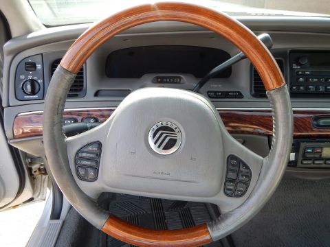 2002 Mercury Grand Marquis - The interior of a 2002 Mercury Grand Marquis features a wood-trimmed steering wheel and a Mercury emblem on the airbag cover.