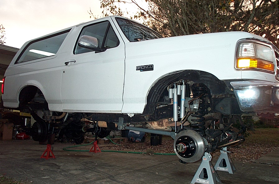 White Ford Bronco on jack stands showing front axle, coil springs and dual shocks