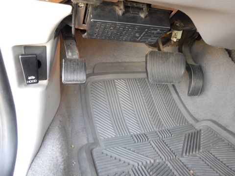 2002 Mercury Grand Marquis - The driver's side footwell of a vehicle, the brake and accelerator pedals, along with the hood release lever and fuse box.