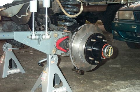 1995 Ford Bronco - Close-up of a Ford Bronco's front axle assembly, supported by jack stands, with another vehicle visible behind it.