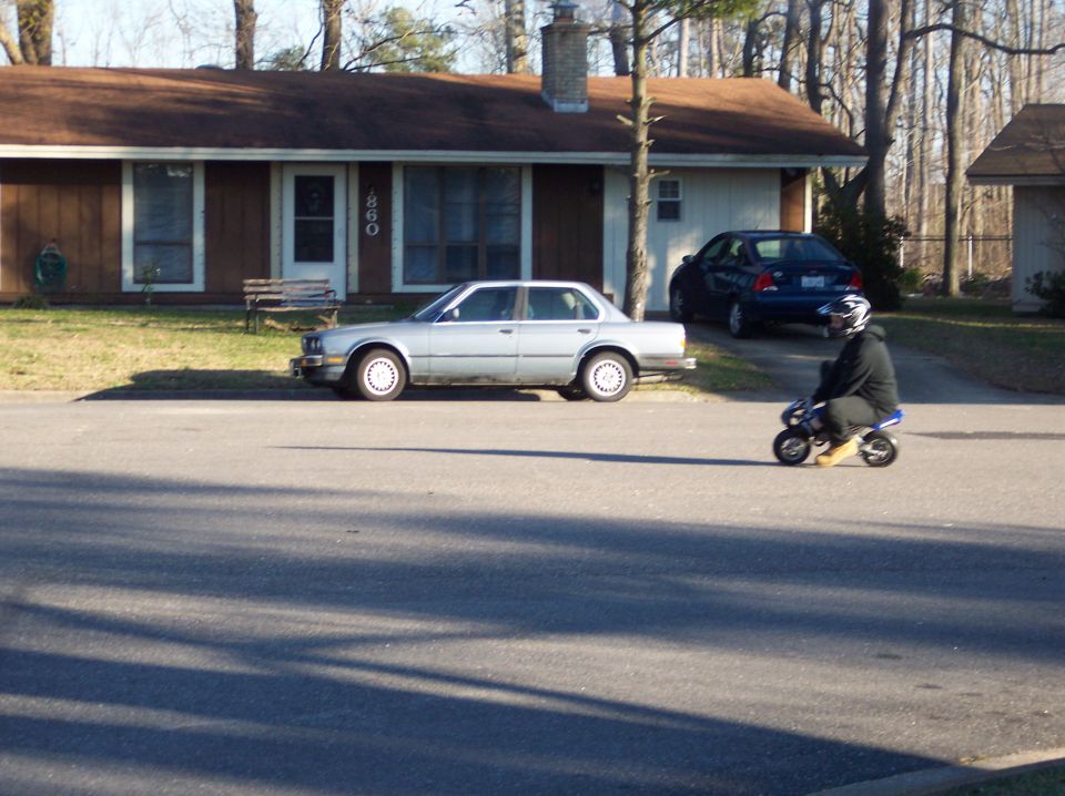 Rider on small blue pocket bike in street, silver BMW 3 Series sedan parked at curb