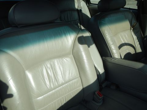 2002 Mercury Grand Marquis - The interior of a car features light-colored leather seats and an armrest, with sunlight streaming in.