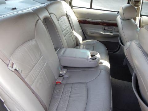 2002 Mercury Grand Marquis - The rear interior of a 2002 Mercury Grand Marquis features light gray leather seats and a fold-down armrest with cup holders.