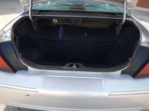 2002 Mercury Grand Marquis - The rear trunk of a silver sedan is open, revealing its carpeted interior space.