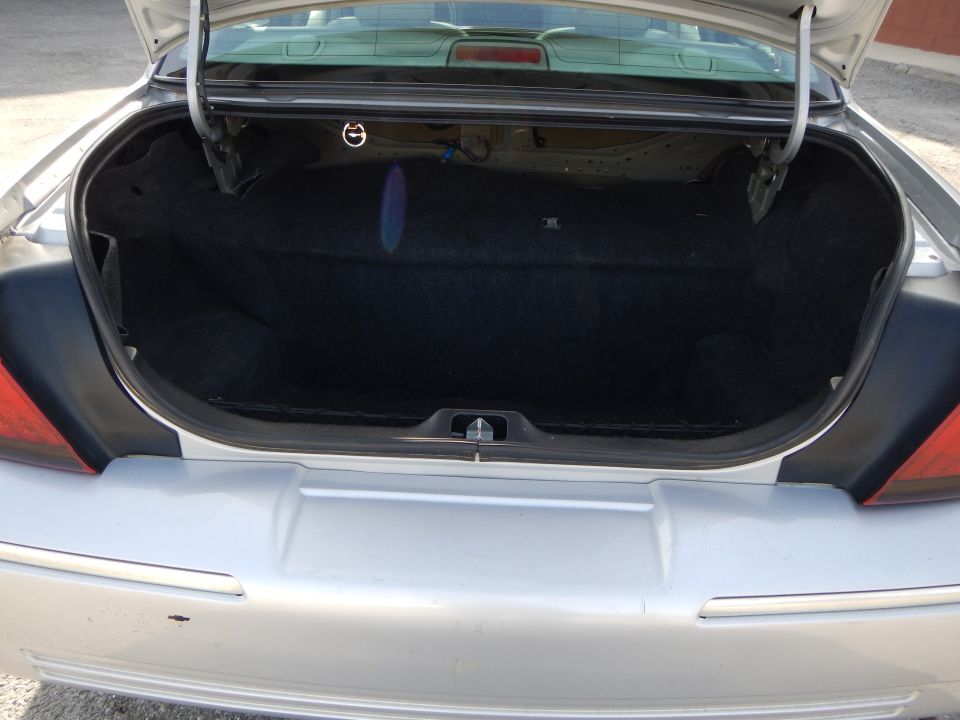 Open trunk of a silver sedan. The trunk is lined with black carpet
