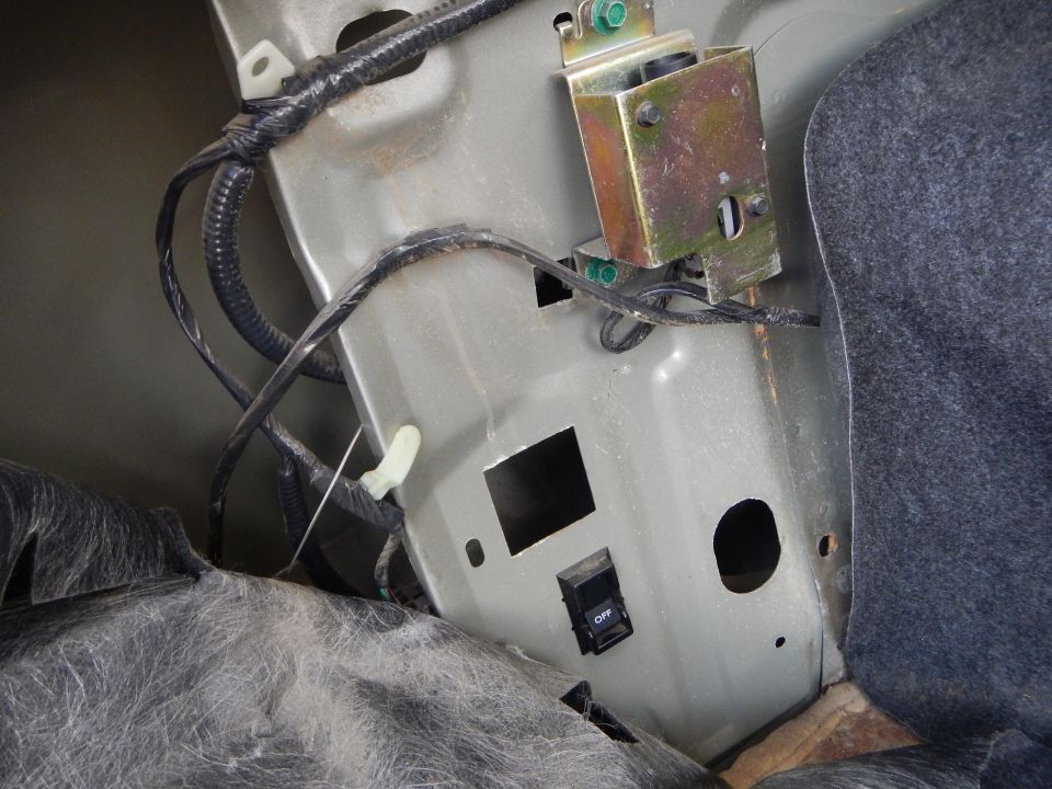 Car trunk interior showing wiring harness, metal bracket, and a black ON/OFF switch