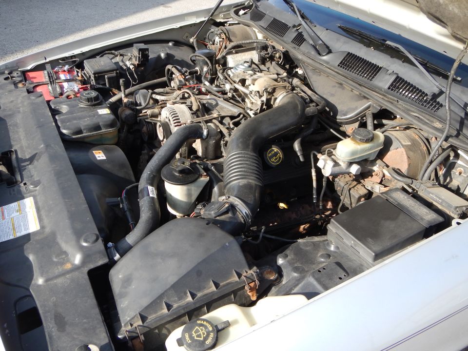 Engine bay of a 2002 Mercury Grand Marquis, showing the V8 engine, battery, and various hoses and components