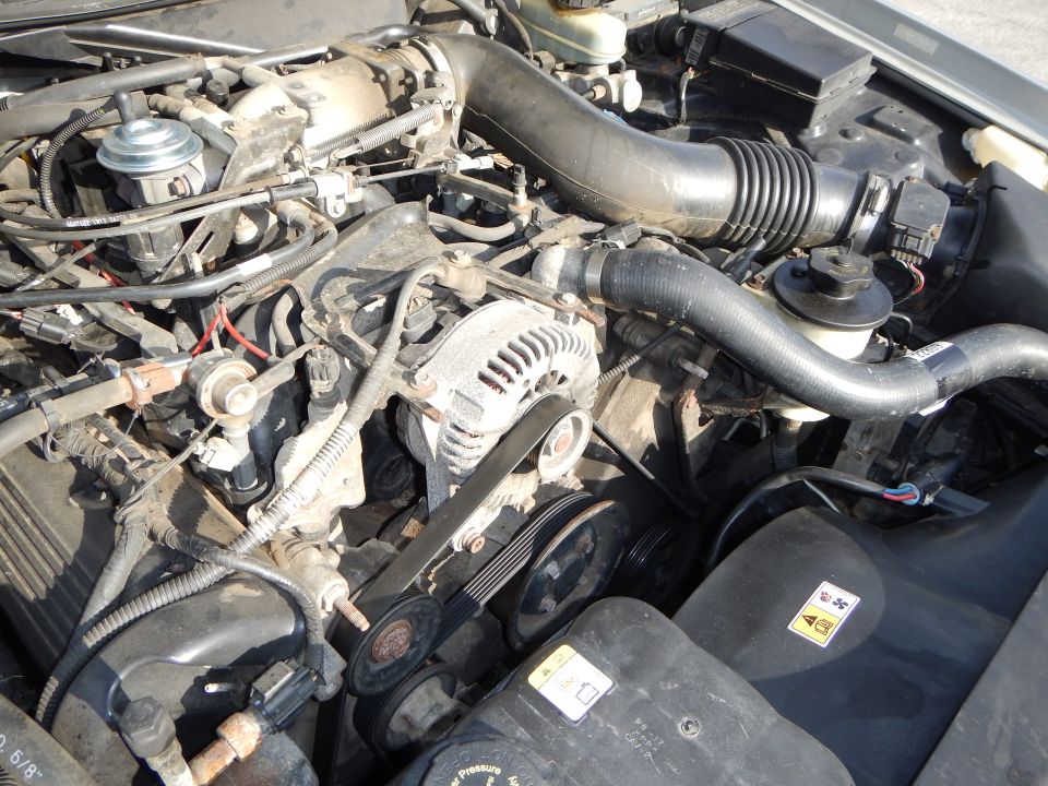 Engine bay with alternator, belts, and hoses visible. Some text on plastic covers