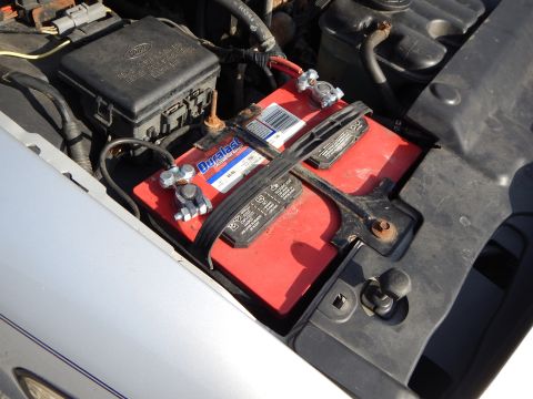 2002 Mercury Grand Marquis - Close-up view of a red Duralast car battery with visible terminals and labeling.
