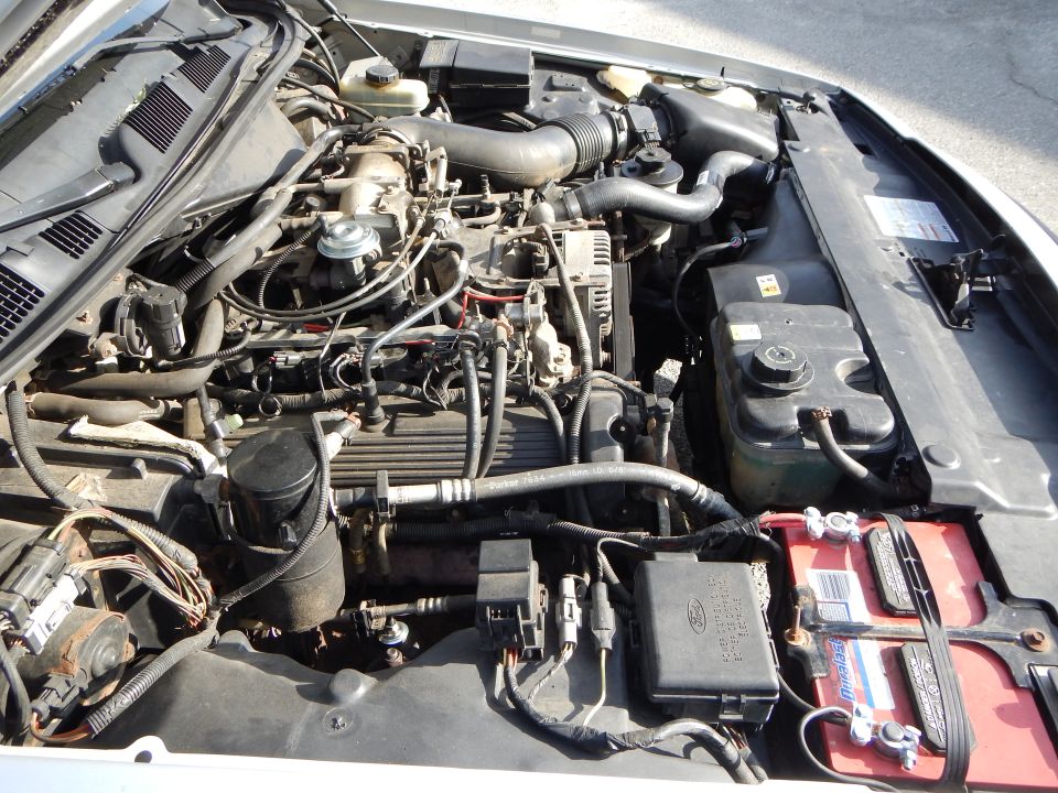 Engine bay with V8 engine, battery, fuse box, and various hoses and wires