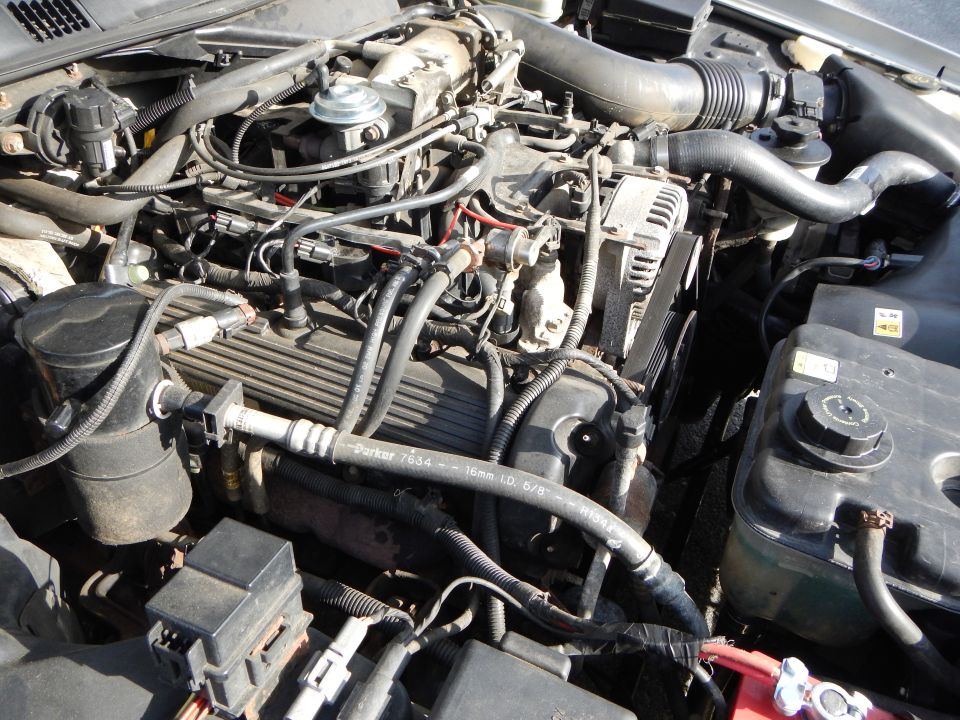 Engine bay with hoses, wiring, alternator, and coolant reservoir visible. Parker hose markings are present