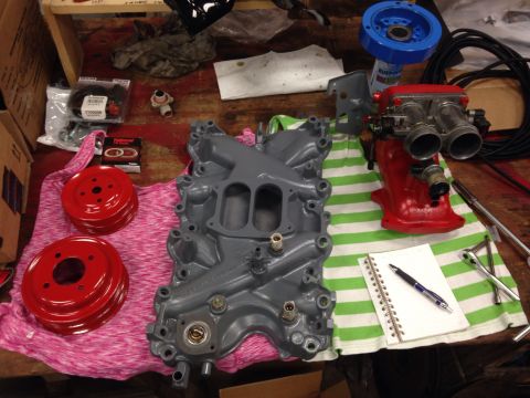 1993 Ford Bronco - Engine parts laid out on a workbench, including an intake manifold, throttle body, and pulleys.