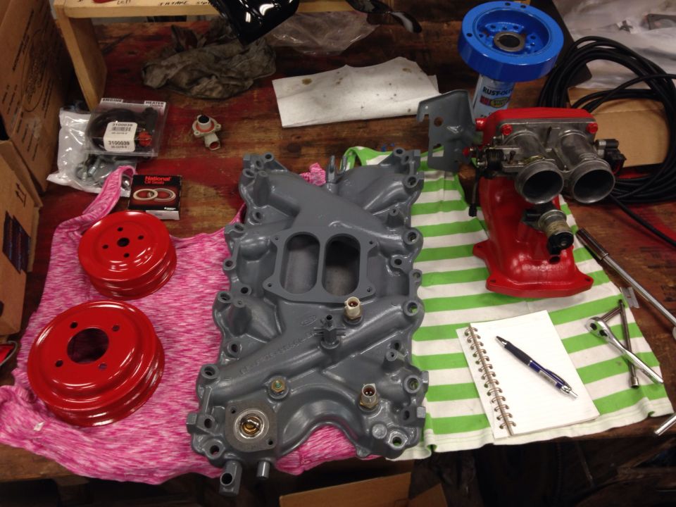 Gray intake manifold and red throttle body with pulleys and a notebook on a workbench