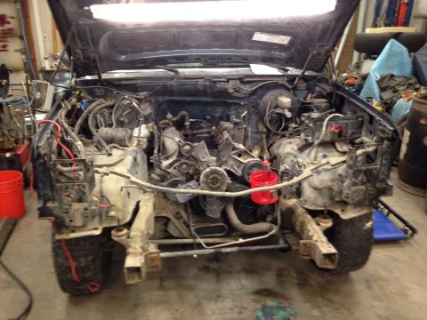 1993 Ford Bronco - The front end of a vehicle is disassembled in a workshop, revealing the engine bay and chassis components.