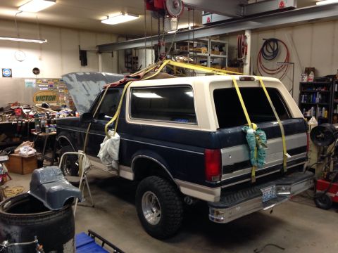 1993 Ford Bronco - A Ford Bronco is suspended by a shop crane, undergoing repairs in a workshop environment.