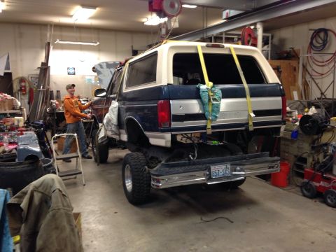 1993 Ford Bronco - A blue and white 1993 Ford Bronco is lifted in a garage, with a person standing nearby.
