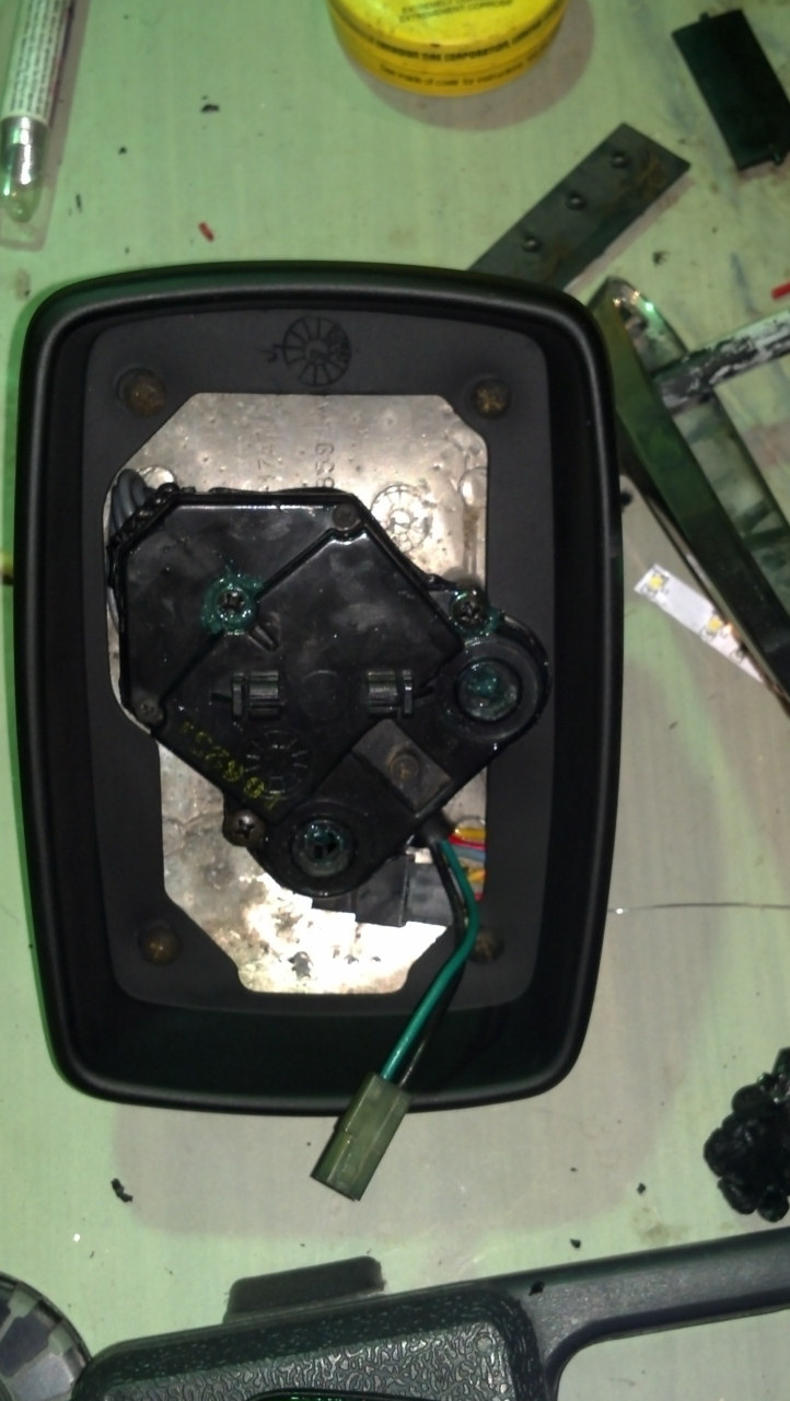 Car mirror assembly with wiring and internal mechanism, disassembled on a workbench
