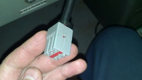 1985 Mercury Grand Marquis - Close-up of a gray electrical connector with red wire inserts, held in a person's hand.