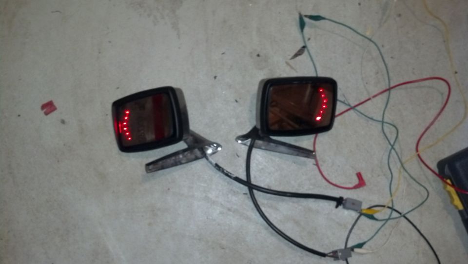 Two car side mirrors with red LED turn signals wired up on a concrete floor