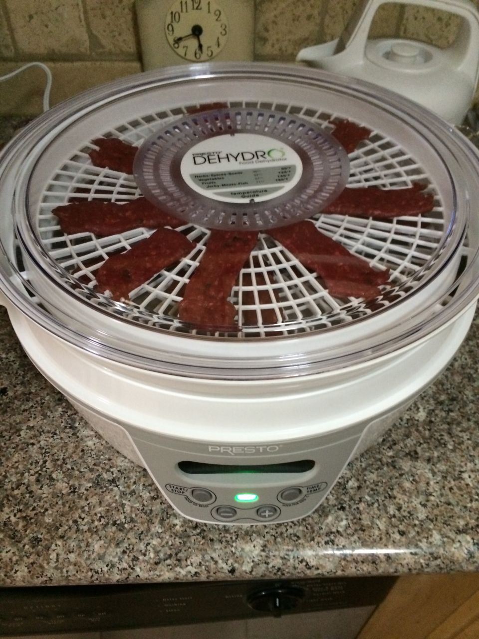 Presto dehydrator with jerky on trays. Clock on wall in background
