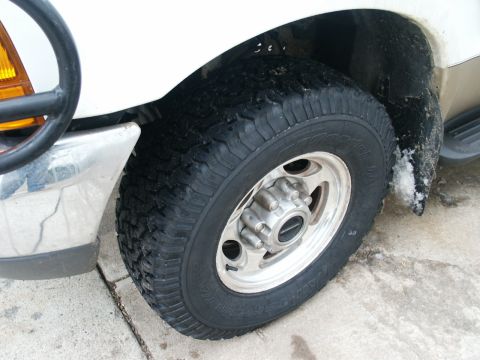 2000 Ford F-250 - The front wheel and fender of a white 2000 Ford F-250 are visible, with a chrome bumper and part of a brush guard.