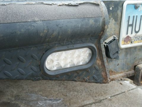 2000 Ford F-250 - Close-up of a worn rear bumper assembly, showing a trailer light and license plate.