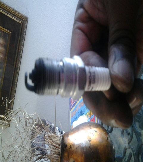 2004 Ford Crown Victoria - A used spark plug is held up for inspection, revealing its condition and some printed text on its side.