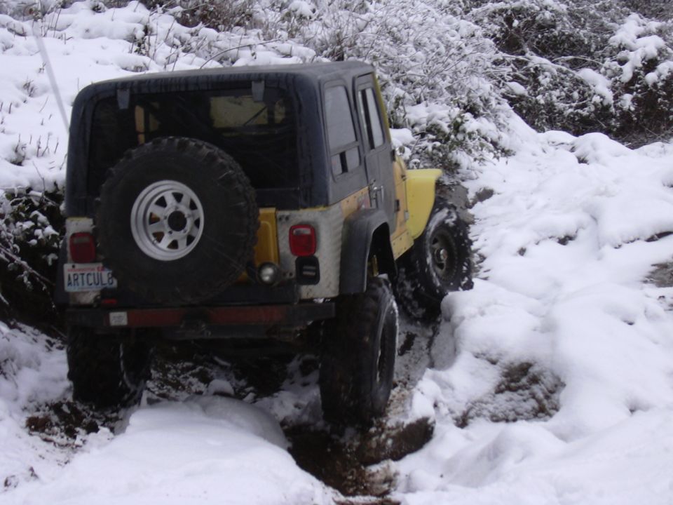 Yellow Jeep Wrangler with hardtop and rear tire carrier crawling a snowy rutted trail