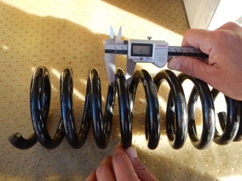 2003 Ford Crown Victoria - black coil spring lies on a perforated tan pad while a hand uses a Mitutoyo digital caliper to measure the wire.