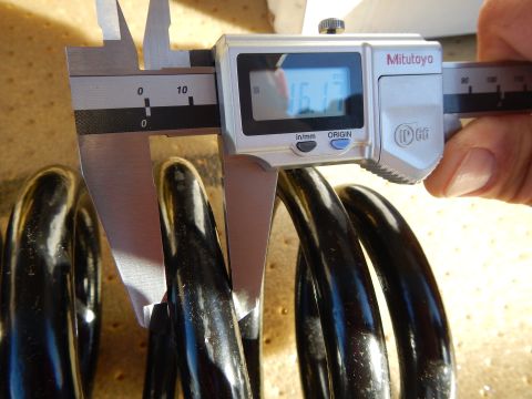 2003 Ford Crown Victoria - hand uses a Mitutoyo digital caliper to measure the wire diameter of a black coil spring on a tan pad.
