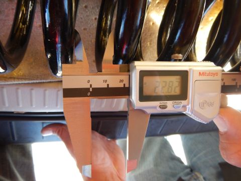 2003 Ford Crown Victoria - hand holds a Mitutoyo digital caliper showing 22.82 to measure the coil gap of a black coil spring.
