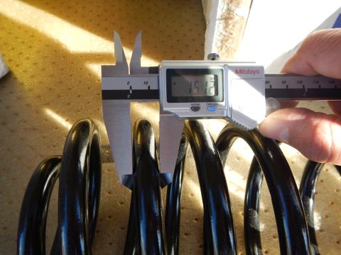 2003 Ford Crown Victoria - hand uses a Mitutoyo digital caliper showing about 15.8 to measure a black coil spring in sunlight.