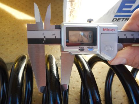2003 Ford Crown Victoria - Mitutoyo digital caliper measures a black coil spring on a tan pad, with an Eaton Detroit Spring box behind.